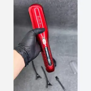 Mano con guante negro sostiene una recortadora inalámbrica de puntas abiertas roja, con pinzas y cepillo al fondo.